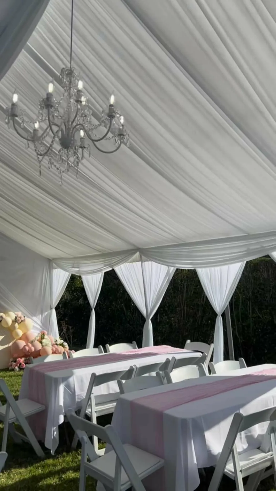 A chandelier suspended from white tent draping above a pink celebration setting