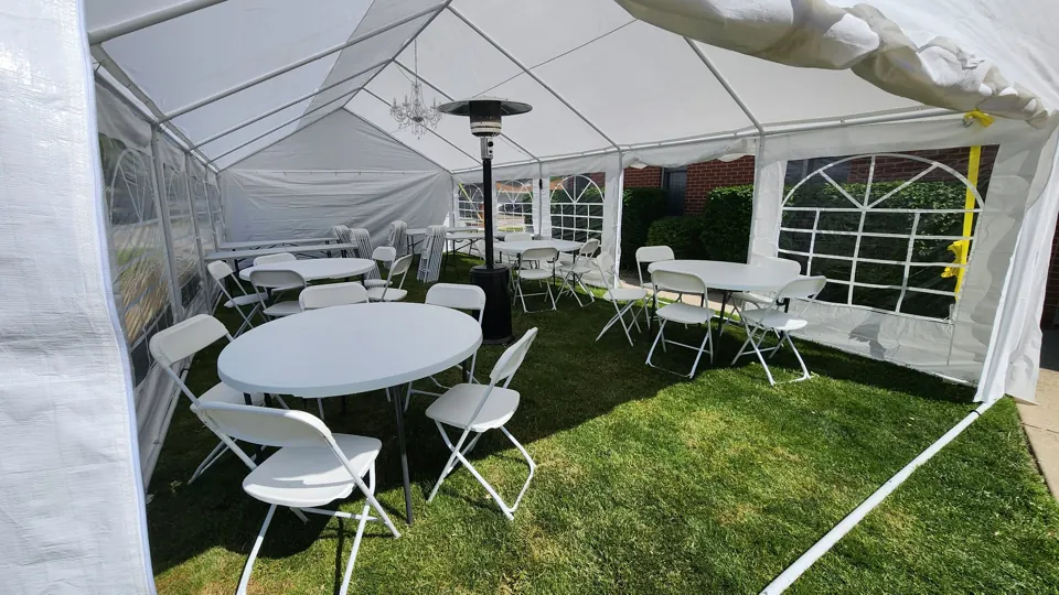 White round tables and folding chairs in a sunny backyard tent installation