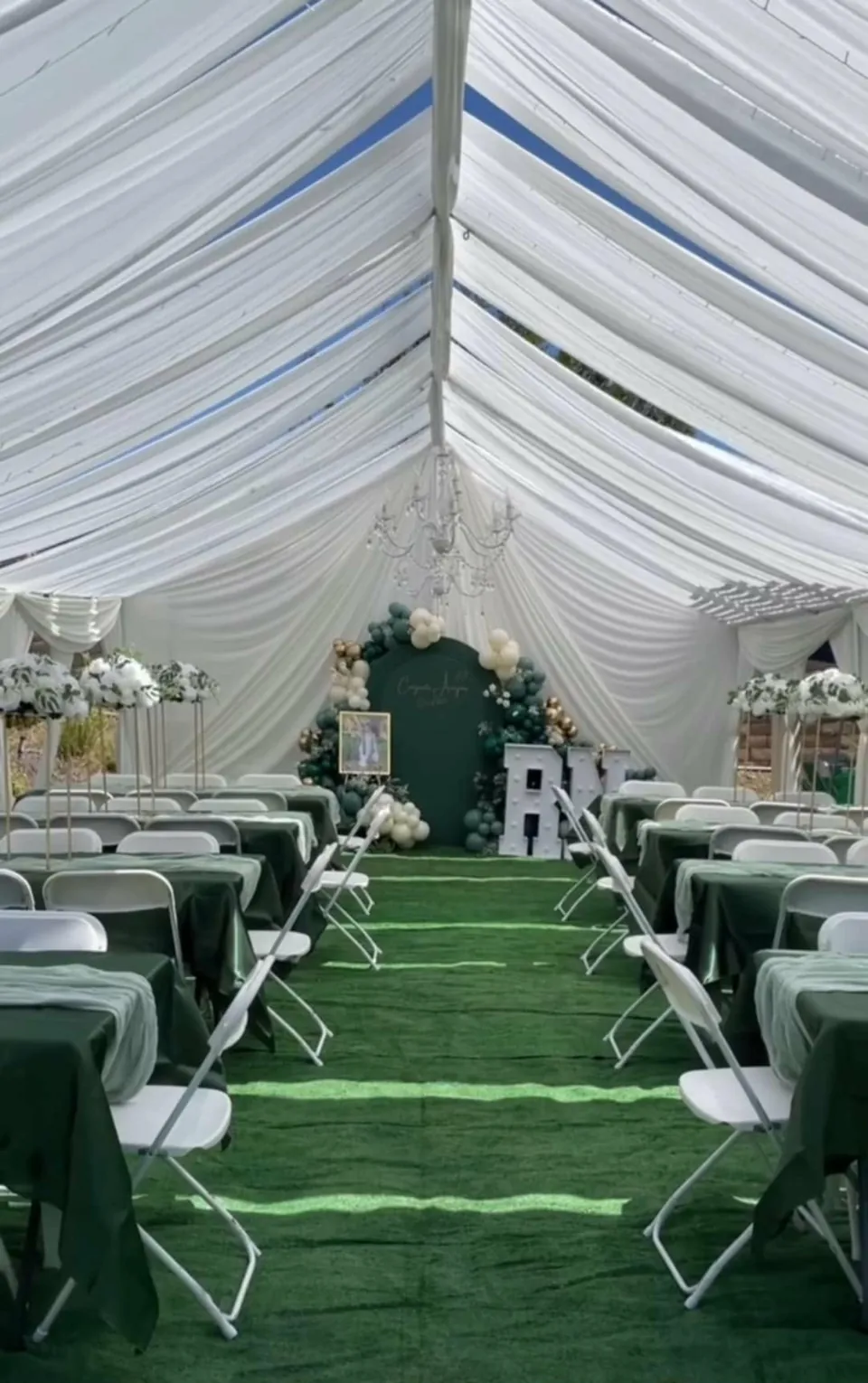 Emerald table linens and white resin garden chairs under gathered white tent draping