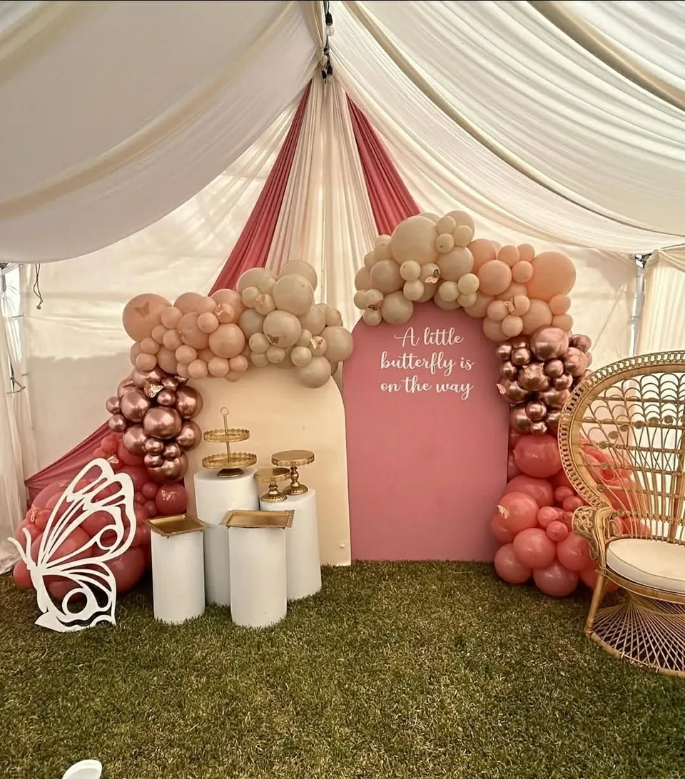 Pink and champagne balloon installation around a butterfly-themed baby shower backdrop