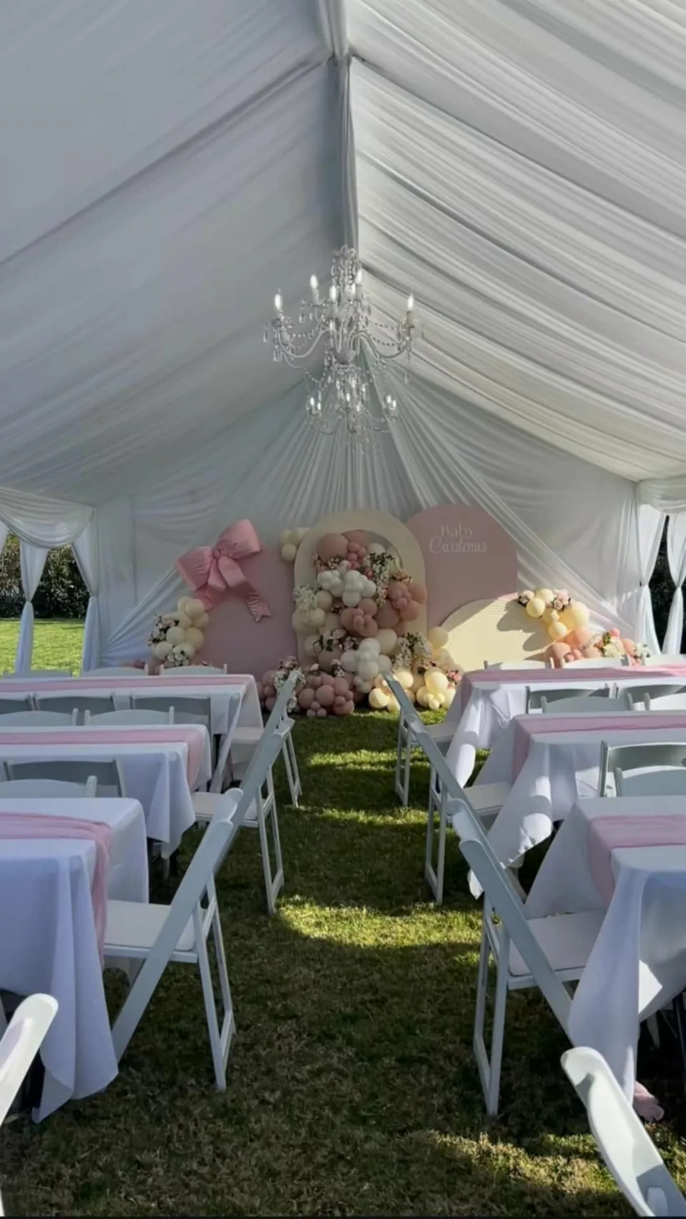 Pink linens, white resin garden chairs and a balloon backdrop in a draped tent