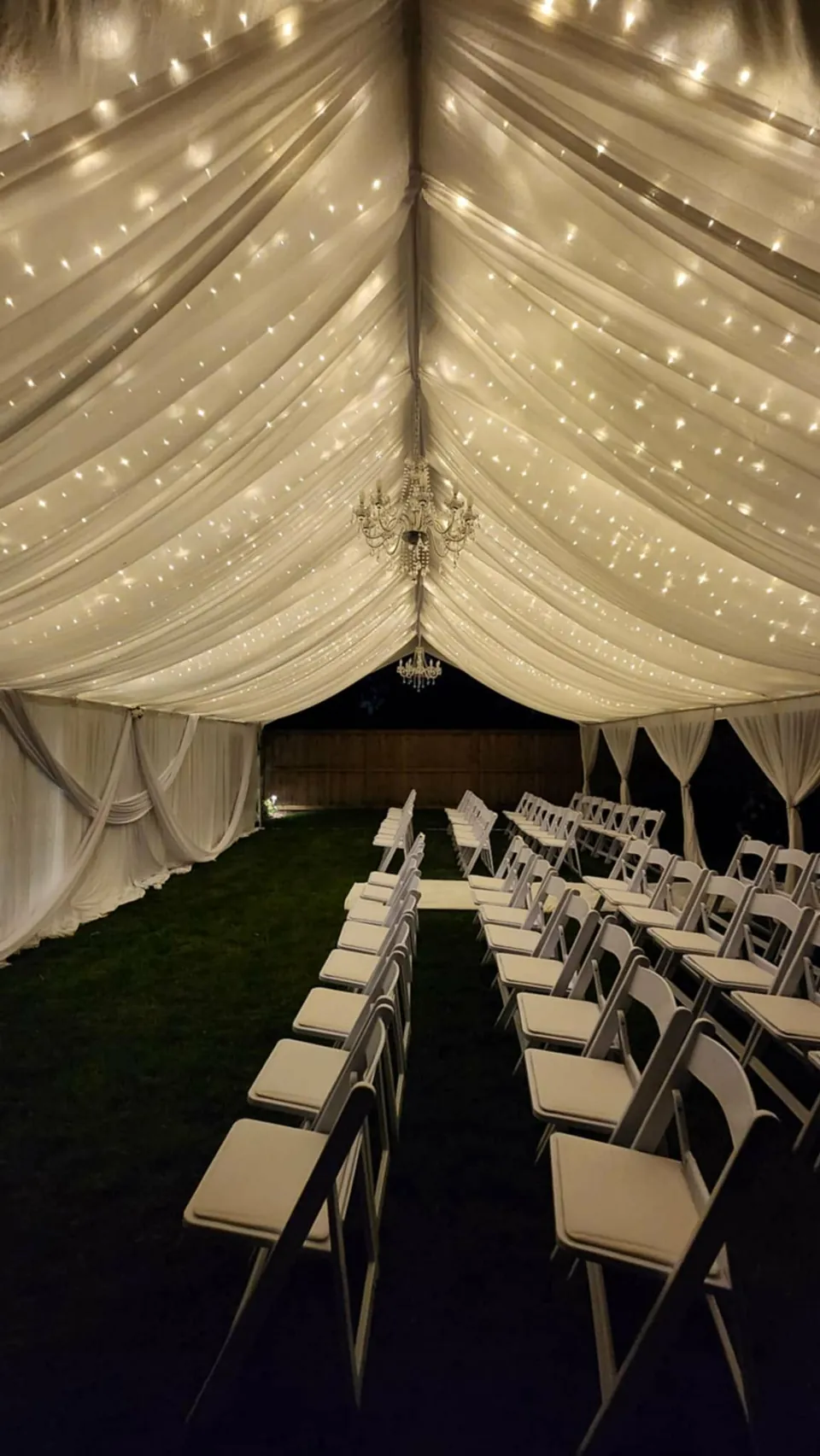 Dinner tables and white chairs beneath a softly lit, fully draped tent ceiling at night